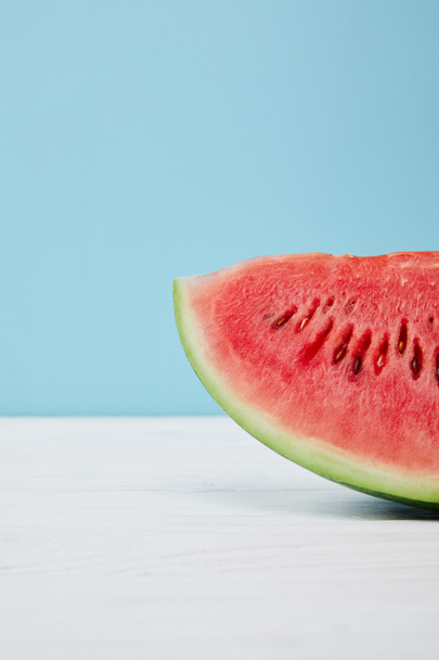 close up view of fresh watermelon slice on white surface on blue background - Zdjęcie, obraz