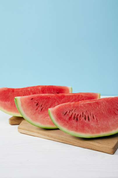close up view of arranged watermelon slices on cutting board on white surface on blue backdrop - Foto, Imagem