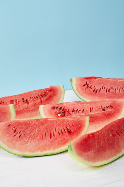 close up view of arranged watermelon slices on white surface on blue backdrop - Foto, afbeelding