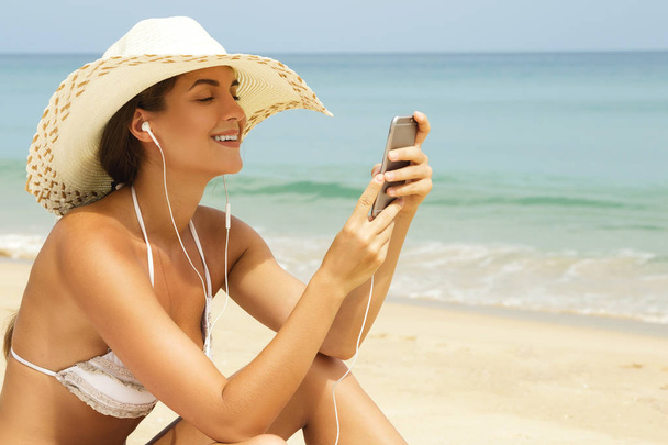 Happy woman wearing hat is listening music on the beach - Φωτογραφία, εικόνα