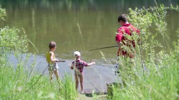 Dwoje małych dzieci i młodych ojciec łowienia ryb w rzece banku. Piękne lato krajobraz. Rekreacji na świeżym powietrzu. - Materiał filmowy, wideo