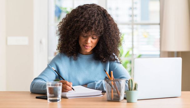 Mujer afroamericana que estudia en casa usando una computadora portátil con una expresión segura en la cara inteligente pensando en serio
 - Foto, imagen
