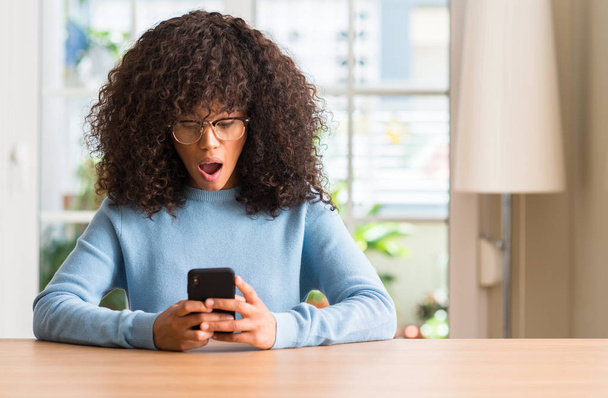 Piękne african american kobieta przy użyciu smartfona przestraszony w szoku ze ścianą niespodzianka, boi się i podekscytowany z wyrazem strachu - Zdjęcie, obraz