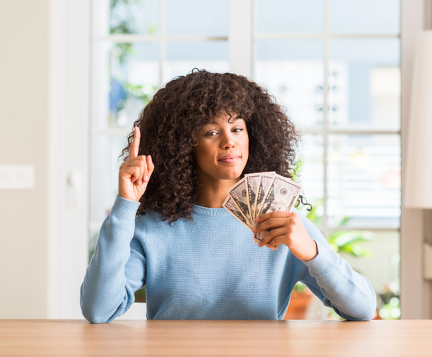 Афро-американських жінка холдингу Долар банк відзначає здивований з ідеєю або питання вказівний палець з щасливим обличчям, номер один - Фото, зображення