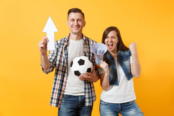 Happy fun expessive couple woman man football fans screaming, cheer up support team with soccer ball, white up arrow, megaphone isolated on yellow background. Sport family leisure lifestyle concept - Фото, изображение