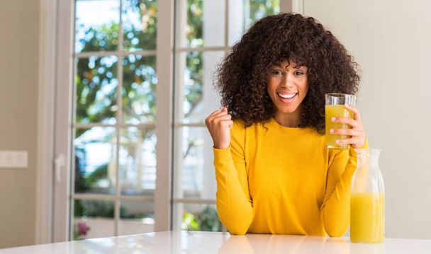 African american woman drinking healthy fruit juice at home screaming proud and celebrating victory and success very excited, cheering emotion - Fotografie, Obrázek