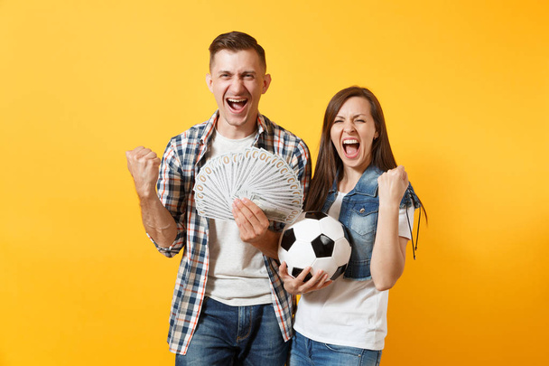 若い勝利カップル、女性男性、サッカーファン ドル、現金、サッカー ボールの束を保持は、黄色の背景に分離されたサポート チームを応援します。スポーツ賭け興奮情熱家族ライフ スタイル コンセプト - 写真・画像