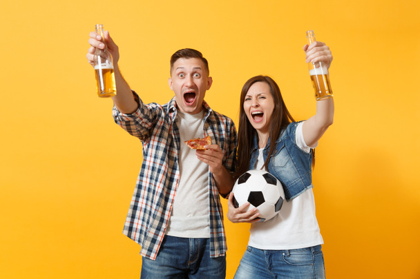 Молодая веселая пара болельщик, женщина мужчина, футбольные болельщики поднять поддержку команды, держа бутылку пива, пиццы ломтик, футбольный мяч изолирован на желтом фоне. Спорт, семейный отдых, концепция образа жизни
 - Фото, изображение