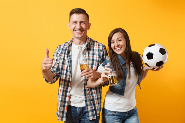 Молодая счастливая веселая пара болельщик, женщина мужчина, футбольные болельщики поднять поддержку команды, держа бутылку пива, футбольный мяч изолирован на желтом фоне. Спорт, семейный отдых, концепция образа жизни людей
 - Фото, изображение