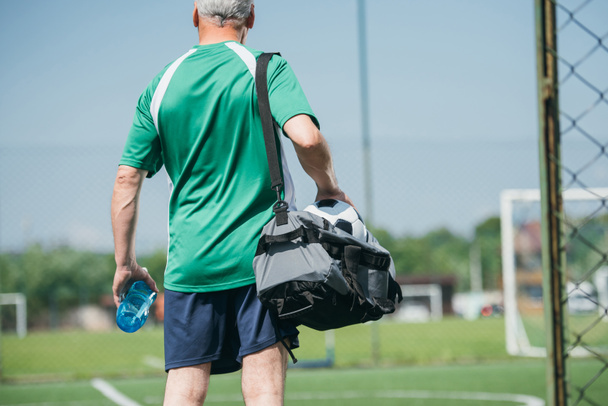 back view of old man with sportive water bottle and bag on soccer field - 写真・画像