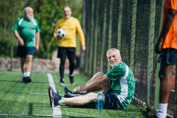 selective focus of interracial elderly football players after match on green field - Photo, Image