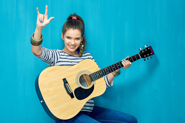 woman holding old guitar and showing rock sign on blue wall background  - Foto, Imagem