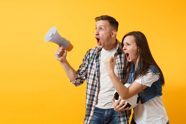 Young happy cheerful couple supporter, woman man, football fans cheer up support team, holding megaphone, soccer ball isolated on yellow background. Sport, family leisure, people lifestyle concept - Fotoğraf, Görsel