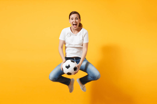 Ekspresyjny kobieta Europejska piłka nożna wentylator skoki zabawa młodych w powietrzu, dopingować zespół wsparcia, trzymając piłki nożnej na białym tle na żółtym tle. Sport, grać w piłkę nożną, dopingować, fanów ludzi lifestyle concept - Zdjęcie, obraz