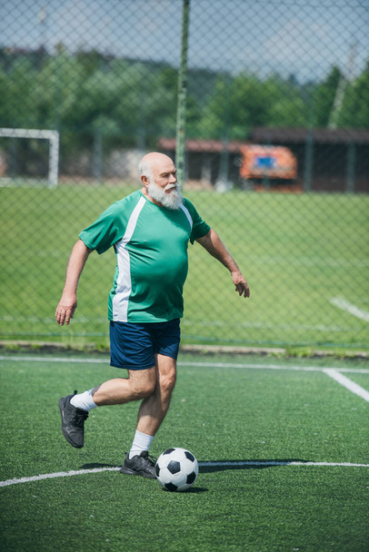 elderly bearded man playing football on field on summer day - Zdjęcie, obraz