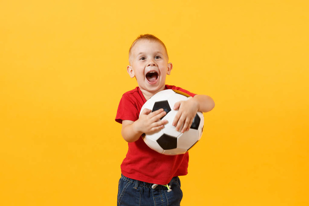 Little cute kid baby boy 3-4 years old, football fan in red t-shirt holding in hand soccer ball isolated on yellow background. Kids sport family leisure lifestyle concept. Copy space advertisement - Foto, Bild