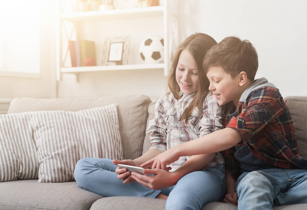 Dos niños jugando en el teléfono inteligente en el sofá en casa
 - Foto, imagen
