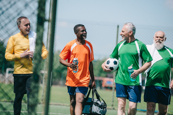 group of interracial elderly sportsmen with sportive water bottles walking on football field - Zdjęcie, obraz