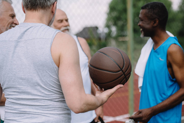 selective focus of group of multiracial old sportsmen with basketball ball on playground - 写真・画像