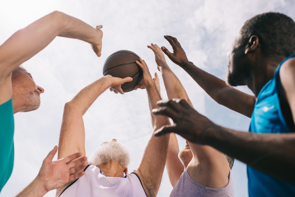 Низкий угол обзора межрасовых пожилых спортсменов, играющих вместе в баскетбол
 - Фото, изображение