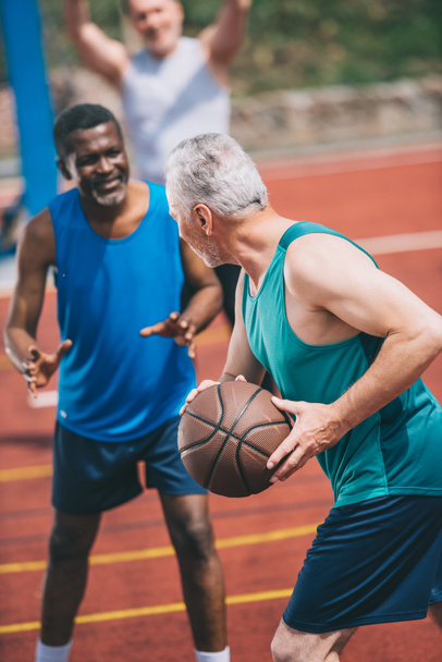 wielorasowe starszych mężczyzn, grając w koszykówkę razem na plac zabaw w letni dzień - Zdjęcie, obraz