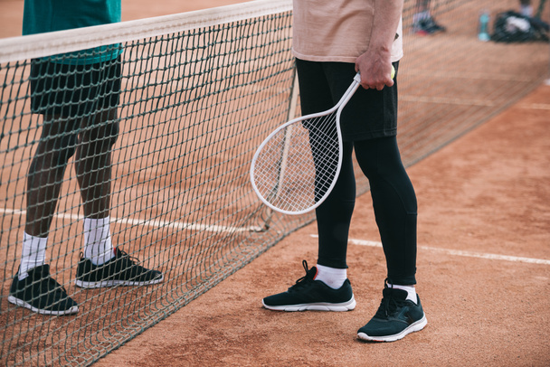 cropped shot of interracial friends with tennis racquet standing near net - Fotó, kép