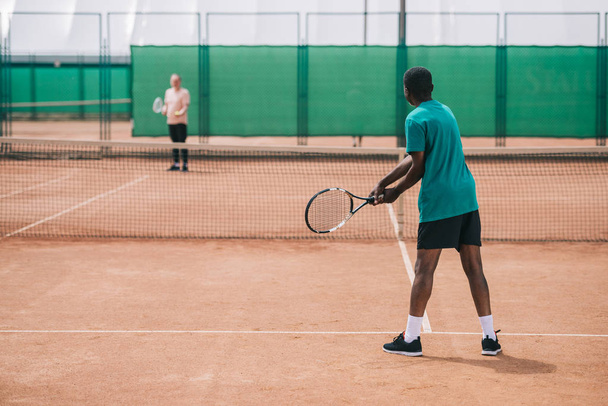 selective focus of elderly african american man playing tennis with friend on court - Фото, изображение