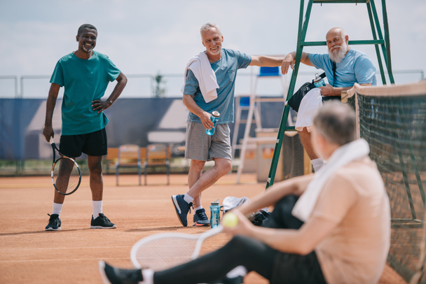 selectieve aandacht van oude multi-etnisch vrienden op tennisbaan op zomerdag - Foto, afbeelding