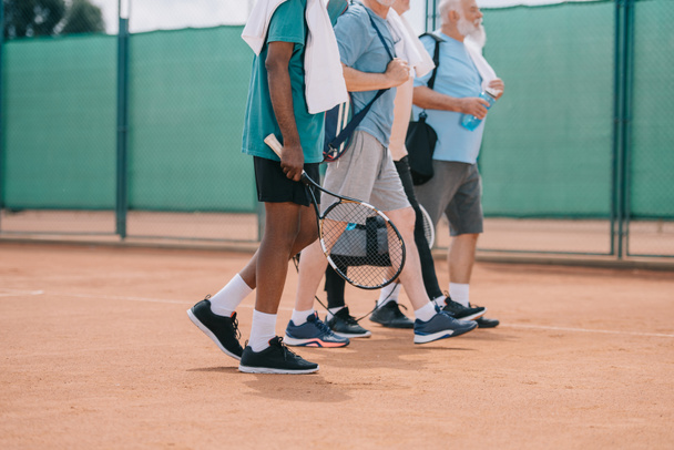 osittainen näkymä monikulttuurinen vanhusten miesten tennisvälineet kävely kentällä
 - Valokuva, kuva
