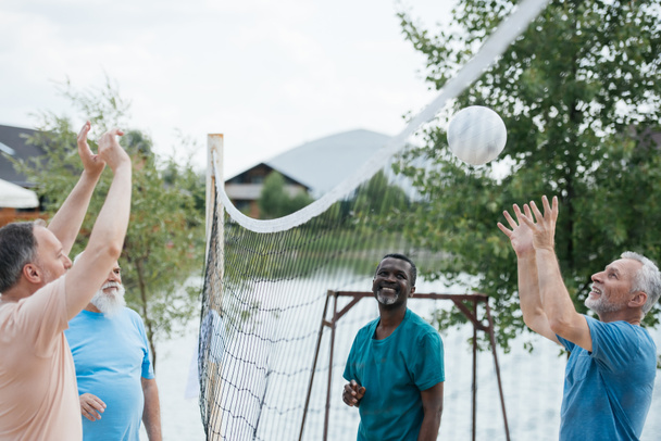 s úsměvem multikulturní staří přátelé hrát volejbal na pláži v letním dni - Fotografie, Obrázek