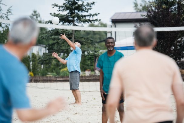 selective focus of multicultural old friends playing volleyball on beach on summer day - Photo, Image