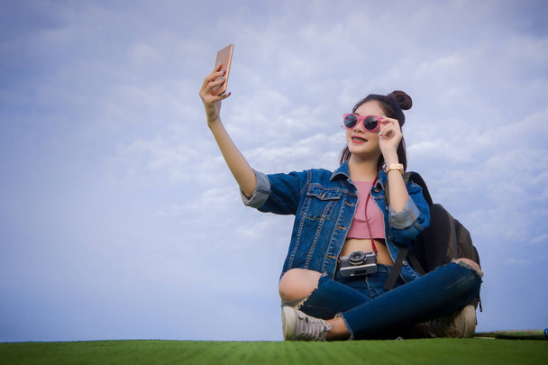 Donna seduta sull'erba verde sorridente il giorno e fotografare lo smartphone selfie
 - Foto, immagini