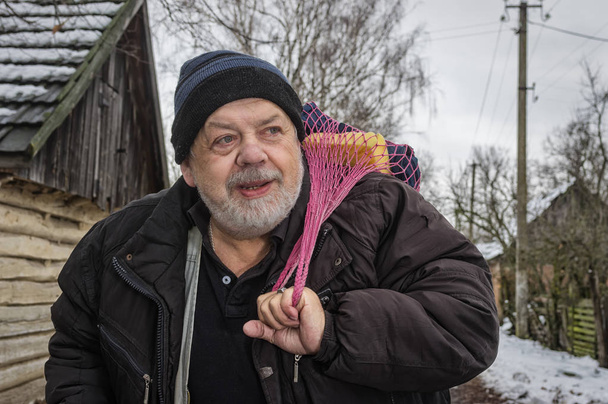 Pozitív ukrán paraszt egy vidéki falu állt, és figyelembe véve a tornazsák a háztartási dolgokat szabadtéri portréja - Fotó, kép