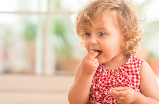 Hermoso niño rubio con ojos azules comiendo dulces en casa
. - Foto, imagen