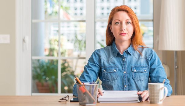 Redhead woman studying at home with a confident expression on smart face thinking serious - Fotoğraf, Görsel