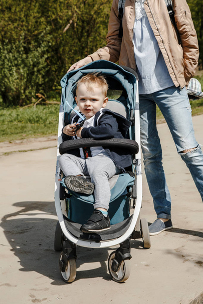 Woman With a baby in a baby carriage. Mother with a little son on a walk. Little boy in a carriage. In street and park. - Фото, изображение