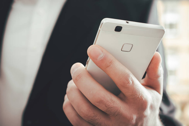 Macro di un uomo d'affari che utilizza uno smartphone di fronte a uno sfondo luminoso
 - Foto, immagini