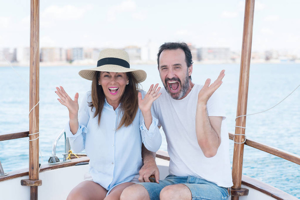 Paar mittleren Alters auf dem Segelboot sehr glücklich und aufgeregt, Siegerausdruck, der Sieg schreiend mit breitem Lächeln und erhobenen Händen feiert - Foto, Bild