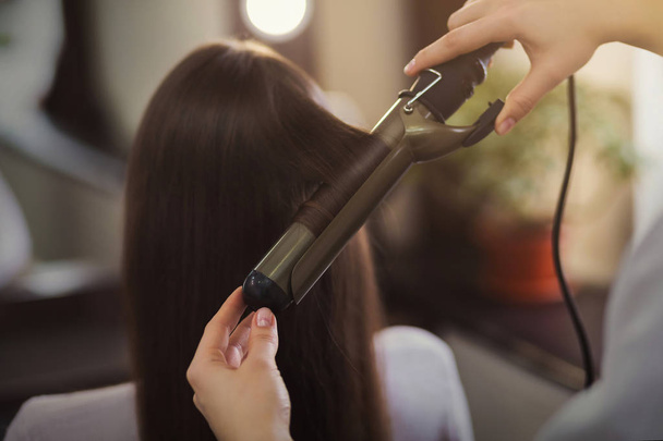 Hairdresser using curling iron at beauty salon - Photo, Image