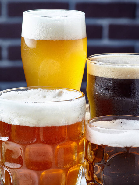 Cuatro vasos con cerveza de diferentes colores y variedades, contra una pared de ladrillo oscuro
. - Foto, imagen