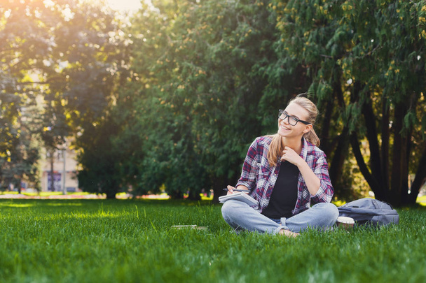 Çim üstünde defter ile oturan genç mutlu kadın - Fotoğraf, Görsel