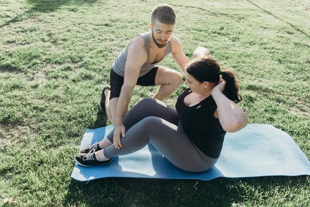 Obese woman doing sit-ups with personal trainer - Foto, afbeelding