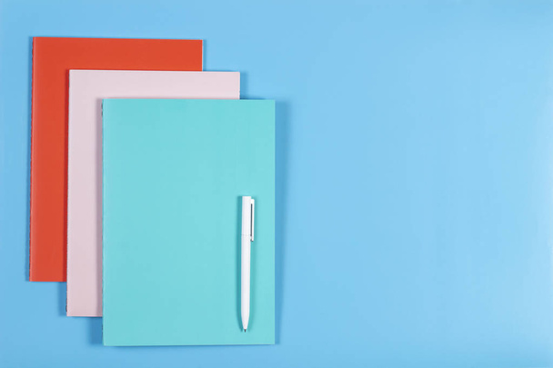 Colorful notebooks and white pen on blue background - Fotó, kép