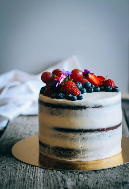 Gâteau au chocolat à la crème crémeuse décoré de fraises, bleuets, raisins et violettes sur fond de bois
 - Photo, image