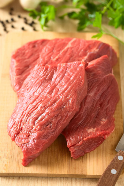 Φρέσκο νωπό βόειο κρέας χωρίς κόκαλα κρέας κομμένο σε φέτες για ξύλινη σανίδα, φωτογραφήθηκε με φυσικό φως (επιλεκτική εστίαση, εστίαση στη μέση της εικόνας) - Φωτογραφία, εικόνα