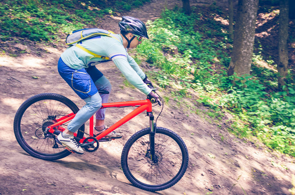 Um ciclista em um capacete desce da montanha em uma bicicleta laranja
. - Foto, Imagem
