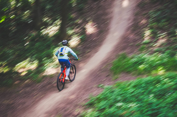 A cyclist in a helmet descends from the mountain on an orange bicycle, motion blur. - Valokuva, kuva