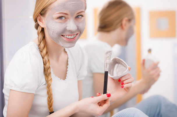 Skincare. Blonde woman in bathroom with gray clay mud mask on her face. Young lady taking care of skin. Spa beauty wellness. - Foto, immagini