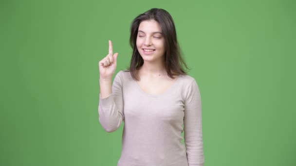 Joven feliz hermosa mujer pensando mientras señala con el dedo hacia arriba
 - Imágenes, Vídeo