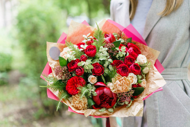 美しい春の花束をもつ少女。赤い牡丹のフラワーアレンジメント。フラワー ショップ、小さな家族経営のコンセプト - 写真・画像